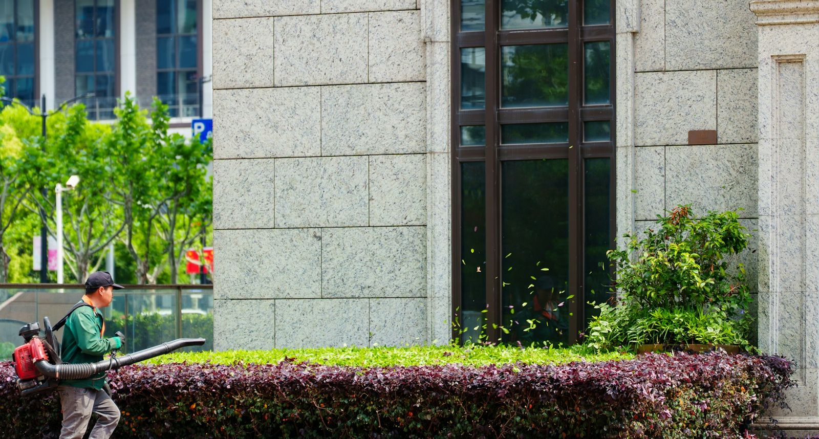 Groundskeeper using a leaf blower beside a commercial building