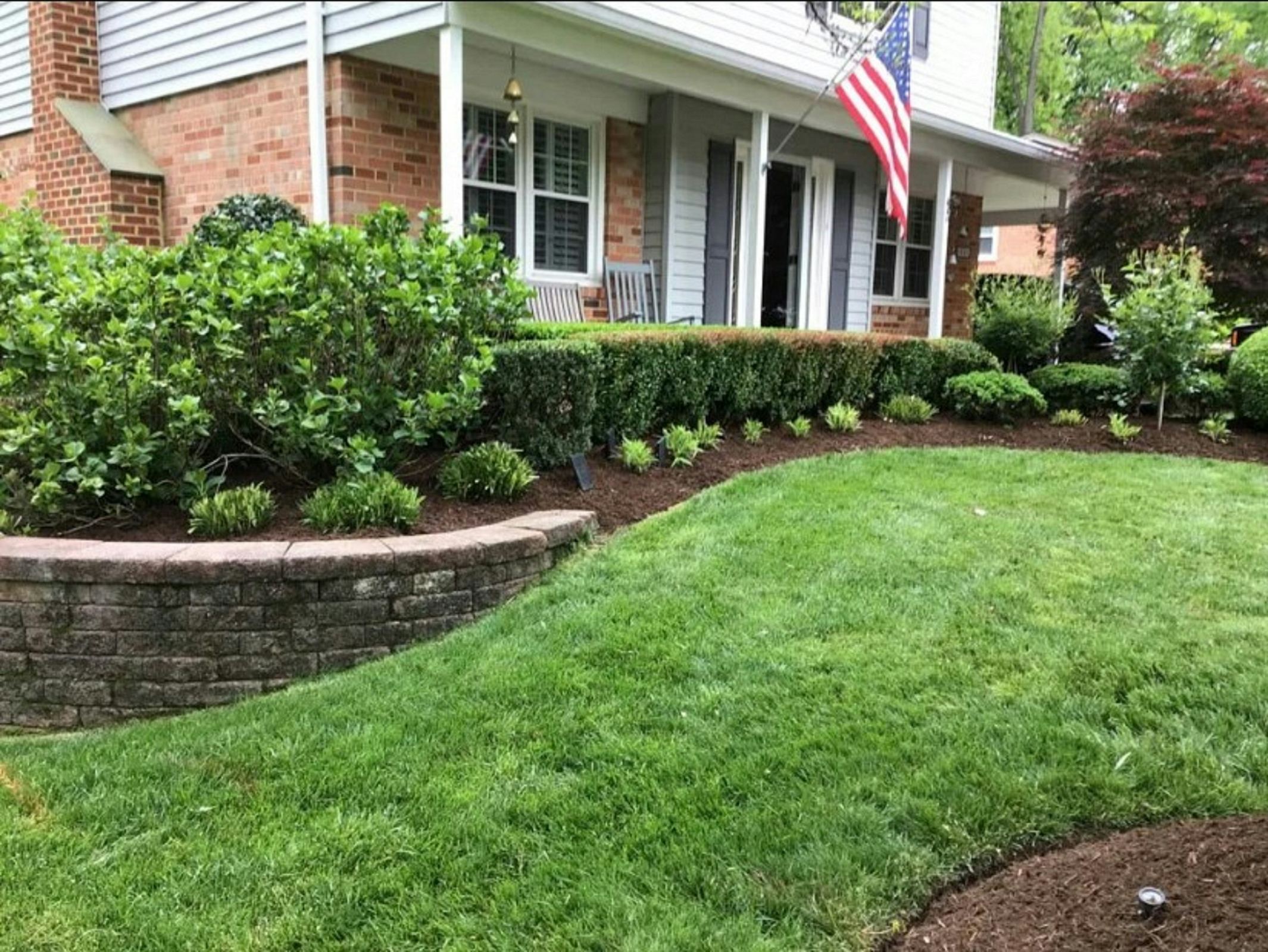 Front lawn with sharp edges along a brick retaining wall and trimmed hedges