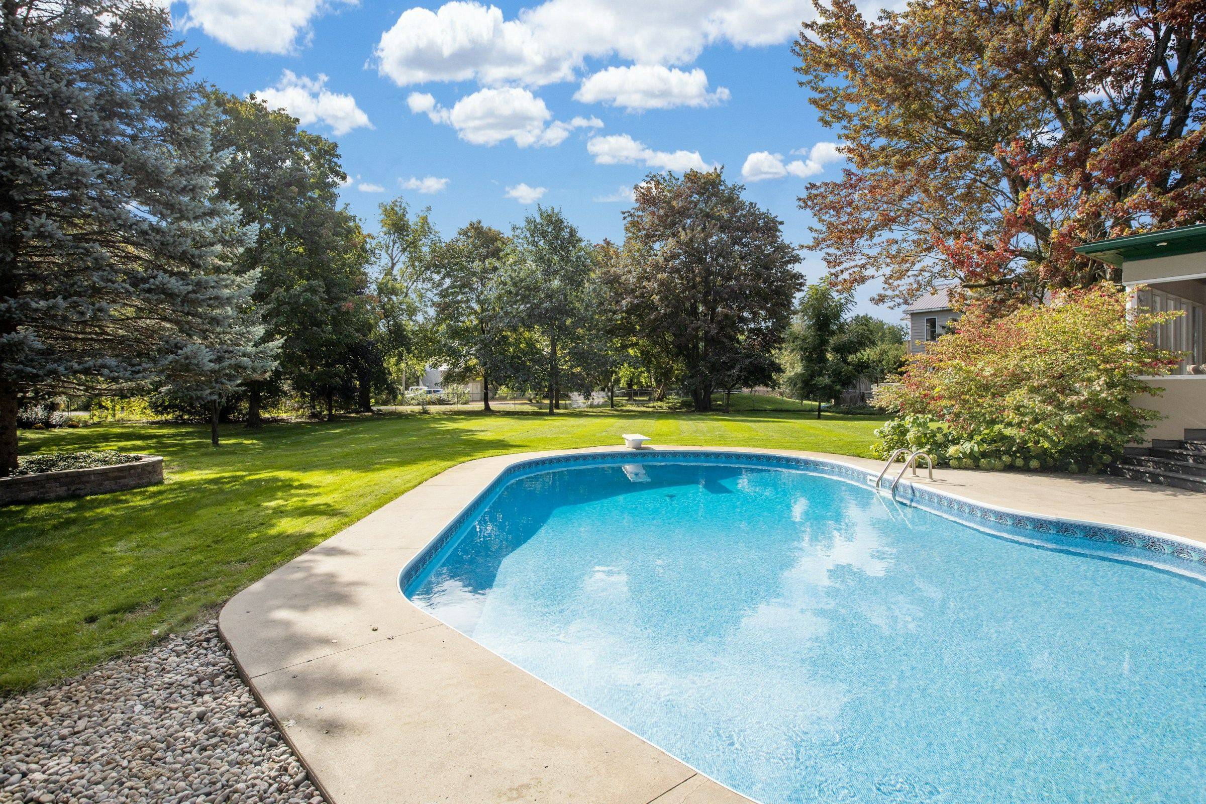 Clear blue backyard pool with a well-kept lawn behind it